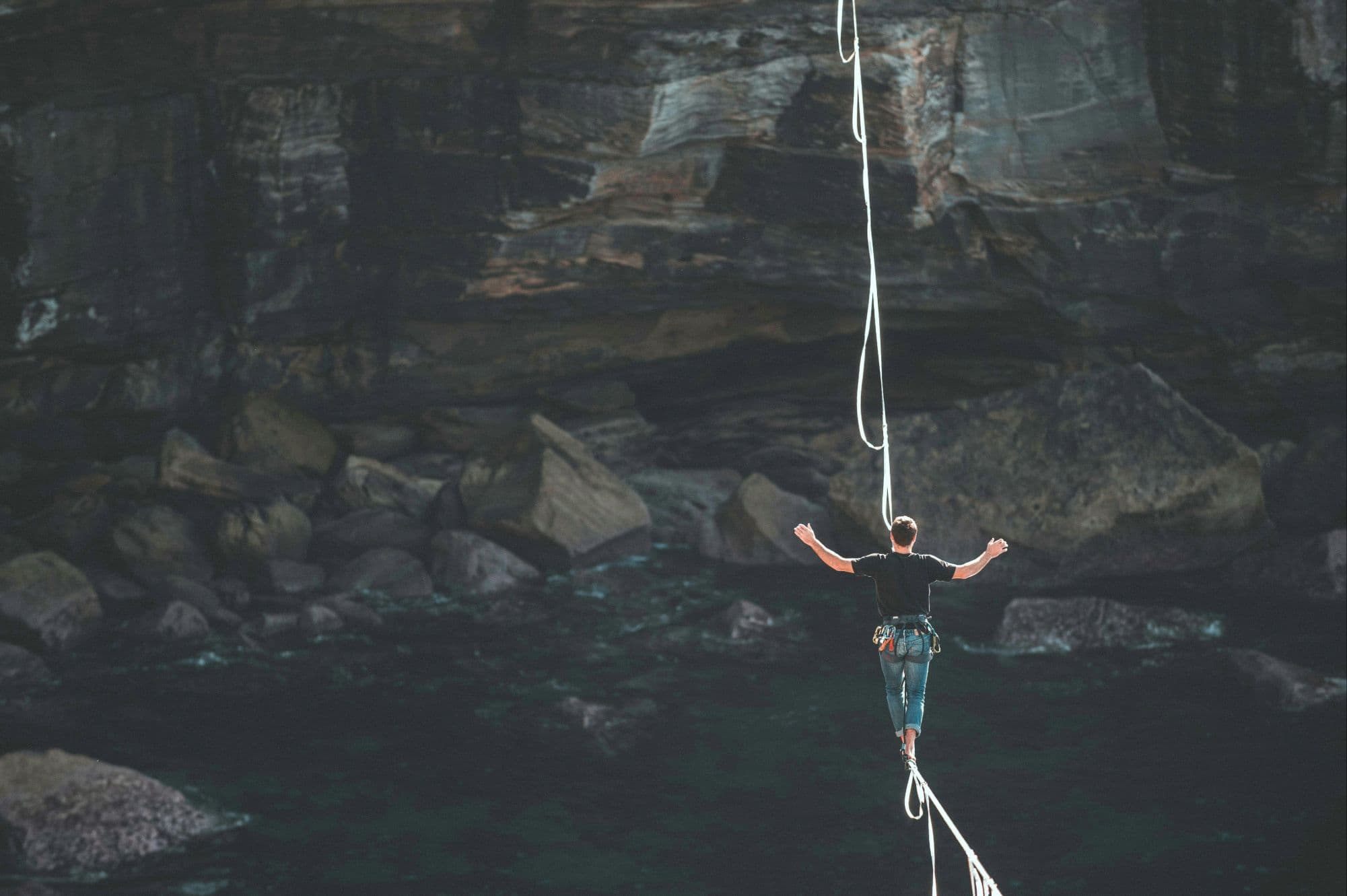 Homme en équilibre sur une highline au-dessus des falaises rocheuses et des eaux profondes, symbolisant les risques de la flexibilité du travail transfrontalier et la frontière ténue entre liberté et conformité.