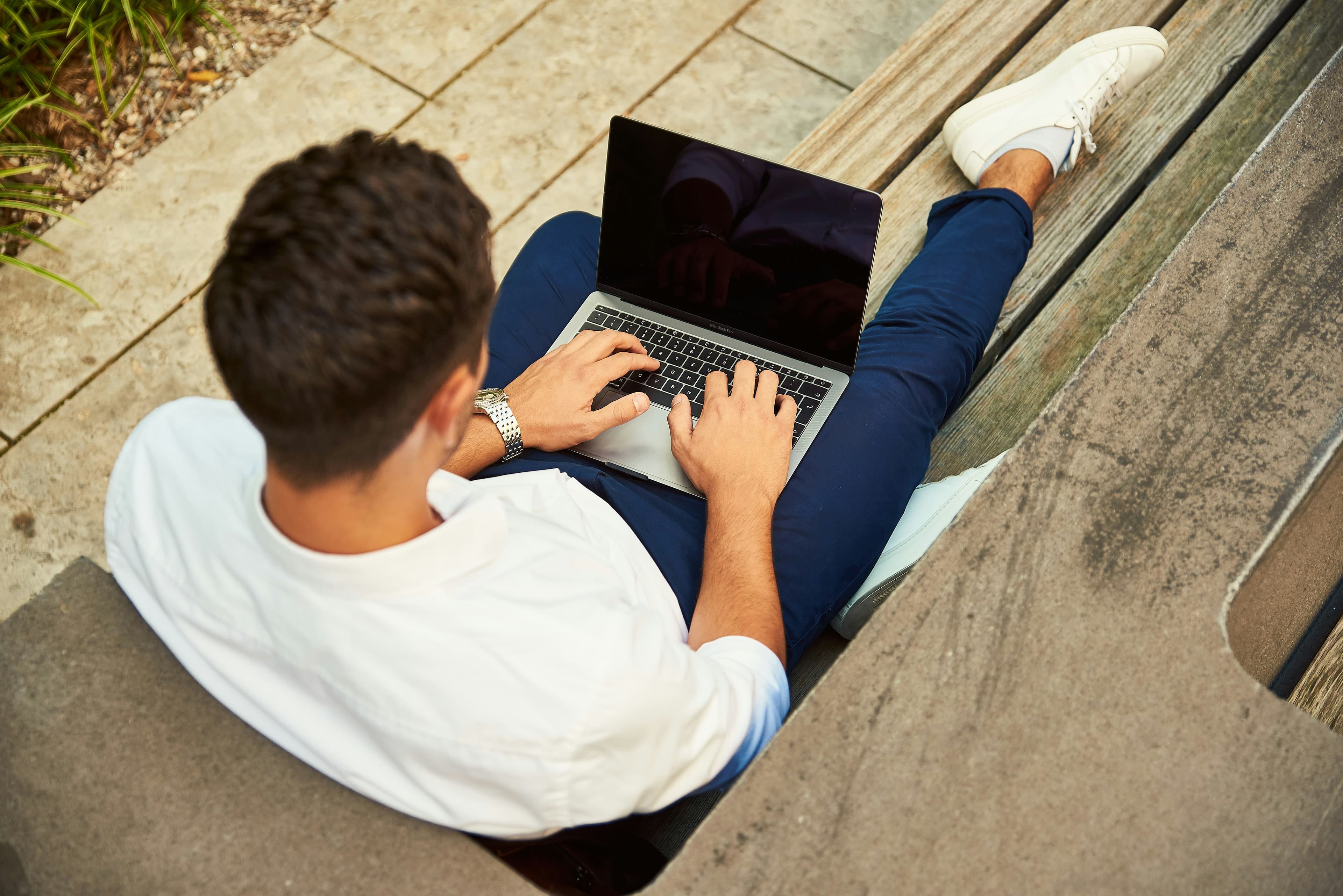 Man sitting on a park bench working on his laptop in a relaxed outdoor setting, symbolizing the balance of work and leisure in the Bleisure lifestyle.