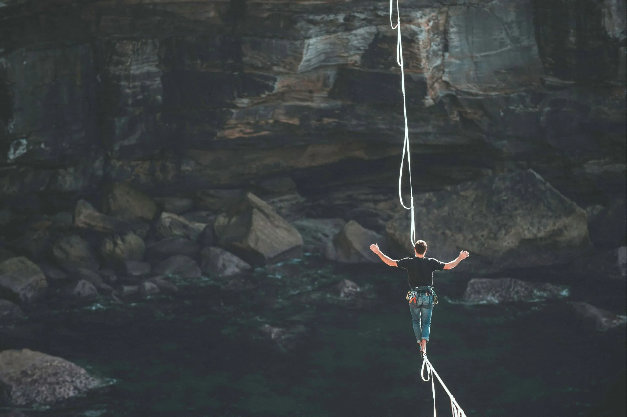 Man balancing on a highline over rocky cliffs and deep water, symbolizing the risks of cross-border work flexibility and the fine line between freedom and compliance.